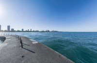 the view of a wide ocean on a sunny day with buildings in the background and a sidewalk leading to the water