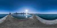 a fish eye view of a dock that leads to the sea with some buildings and the city skyline behind it