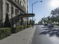 view of an empty city street from the sidewalk and on the sidewalk there are cars going past a building