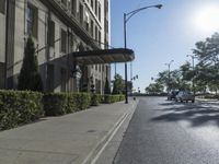 view of an empty city street from the sidewalk and on the sidewalk there are cars going past a building