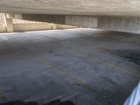 a parking garage with concrete walls and flooring with yellow stripes, near a white car in the foreground