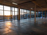 a long empty warehouse with floor to ceiling glass windows and a sunrise in the background