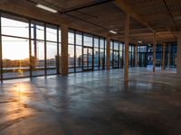 a long empty warehouse with floor to ceiling glass windows and a sunrise in the background