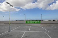 a parking lot with parking spaces and lots of sky lights around the parking lot, there is a green sign indicating an exit to a shop