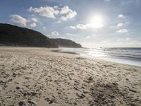 a photo taken on a sandy beach with footprints left in the sand and hills in the background