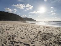 a photo taken on a sandy beach with footprints left in the sand and hills in the background