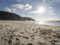 a photo taken on a sandy beach with footprints left in the sand and hills in the background