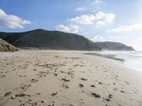 a photo taken on a sandy beach with footprints left in the sand and hills in the background