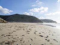 a photo taken on a sandy beach with footprints left in the sand and hills in the background