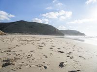 a photo taken on a sandy beach with footprints left in the sand and hills in the background