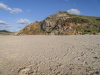 a photo taken on a sandy beach with footprints left in the sand and hills in the background