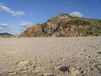 a photo taken on a sandy beach with footprints left in the sand and hills in the background