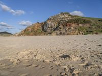 a photo taken on a sandy beach with footprints left in the sand and hills in the background