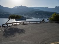 the empty parking lot is located near the mountain shore with an empty road running alongside