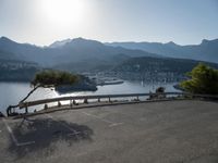 the empty parking lot is located near the mountain shore with an empty road running alongside