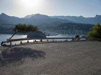 the empty parking lot is located near the mountain shore with an empty road running alongside