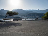 the empty parking lot is located near the mountain shore with an empty road running alongside