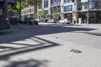 a city sidewalk with parked cars and tall buildings behind it's windows and shadows