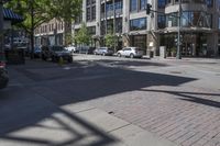 a city sidewalk with parked cars and tall buildings behind it's windows and shadows