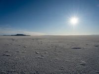 the sun is shining behind some footprints of people walking on an ice covered field of snow