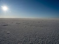 the sun is shining behind some footprints of people walking on an ice covered field of snow