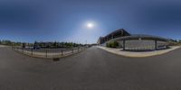 a view looking into the sun over an empty street with some parked cars and an overhang and a building