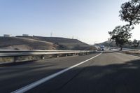 a semi is driving along a freeway near a hill and a road with several cars