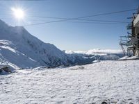 a ski lift going uphill in the mountain next to the snow capped mountains with blue sky