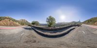 this 360 - pano photo shows a scenic highway on a sunny day with a skateboarder