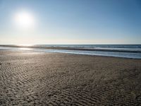 a lone person with a surfboard in the sunlight on a beach area with a body of water