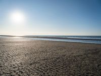 a lone person with a surfboard in the sunlight on a beach area with a body of water