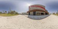 a panoramic photograph of a restaurant across from a park bench with trees in the background