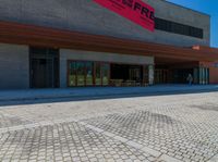 a man on a bicycle riding on a paved driveway near a building and several benches