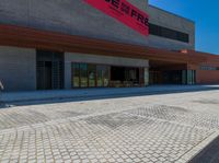 a man on a bicycle riding on a paved driveway near a building and several benches