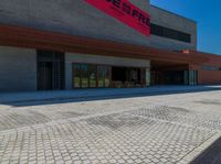 a man on a bicycle riding on a paved driveway near a building and several benches