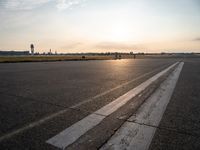 the plane is parked at the end of an airport runway at sunset near a grassy field