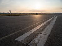 the plane is parked at the end of an airport runway at sunset near a grassy field