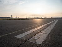 the plane is parked at the end of an airport runway at sunset near a grassy field