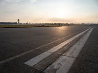 the plane is parked at the end of an airport runway at sunset near a grassy field