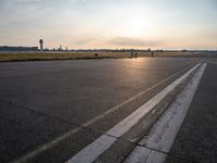 the plane is parked at the end of an airport runway at sunset near a grassy field