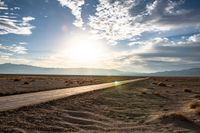 a gravel road runs through the desert with a setting sun behind it on the horizon