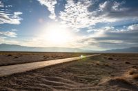 a gravel road runs through the desert with a setting sun behind it on the horizon