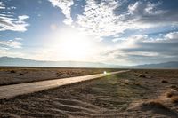 a gravel road runs through the desert with a setting sun behind it on the horizon