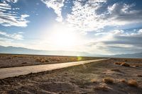 a gravel road runs through the desert with a setting sun behind it on the horizon