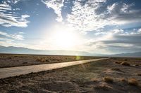 a gravel road runs through the desert with a setting sun behind it on the horizon