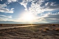 a gravel road runs through the desert with a setting sun behind it on the horizon