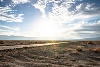 a gravel road runs through the desert with a setting sun behind it on the horizon