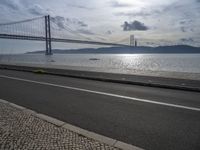 a road leading to an underpass with the forth bridge in the background and a body of water at the far end