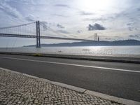 a road leading to an underpass with the forth bridge in the background and a body of water at the far end