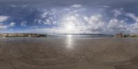 a view of a beach in front of the ocean and clouds from a fish eye lens